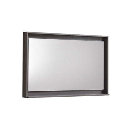 A gray oak framed mirror with a shelf below it.